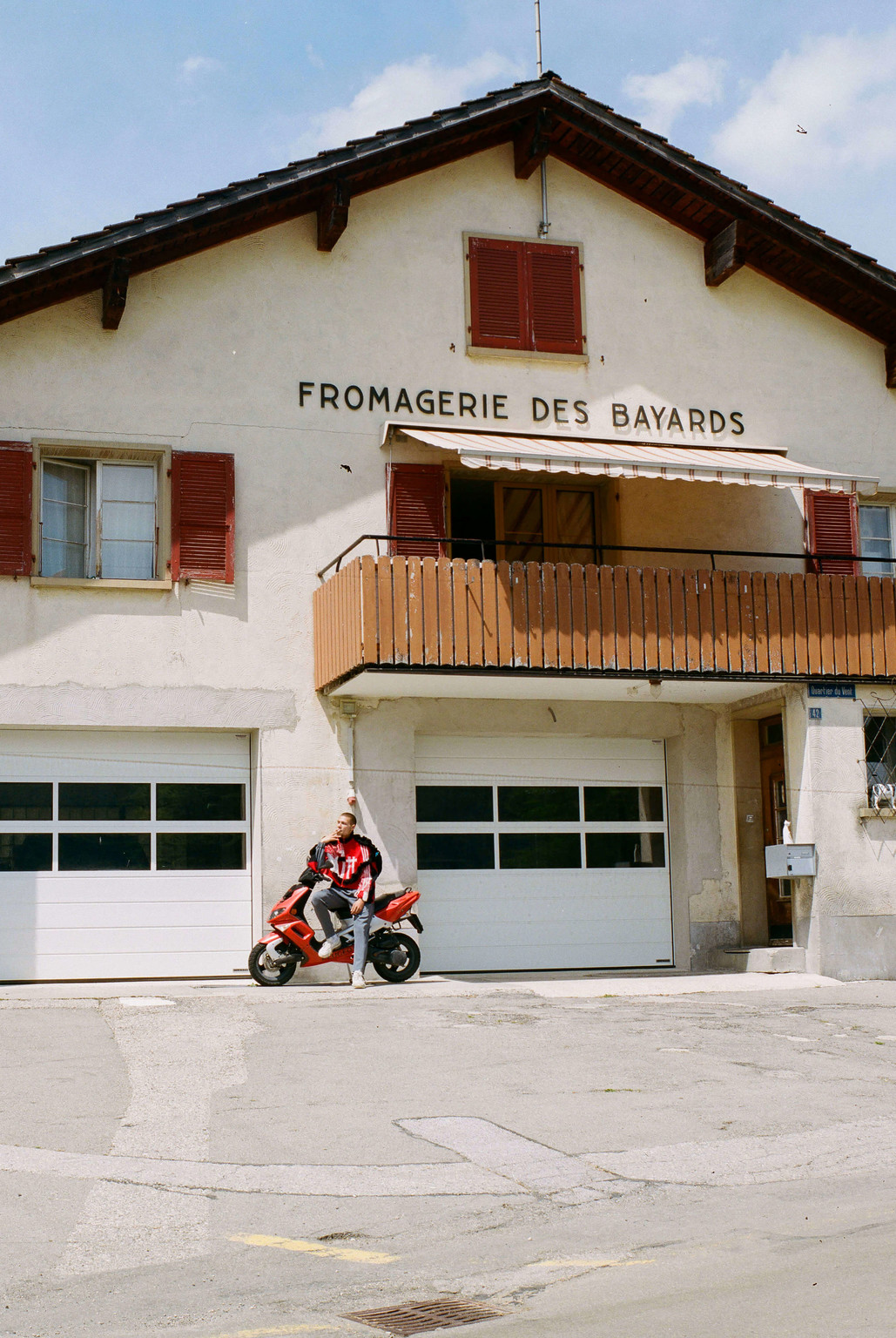 An image from the collection “CH 2127 Les Bayards” by Bryan Colò, who takes a satirical angle to talk about his origins. Here, the model is shot in front of the local dairy - © Photograph: Cynthia Mai Amman, Swiss Design Awards Blog